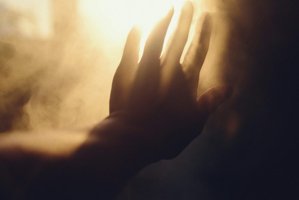 Une main tendue vers une lumière vive à travers la fumée